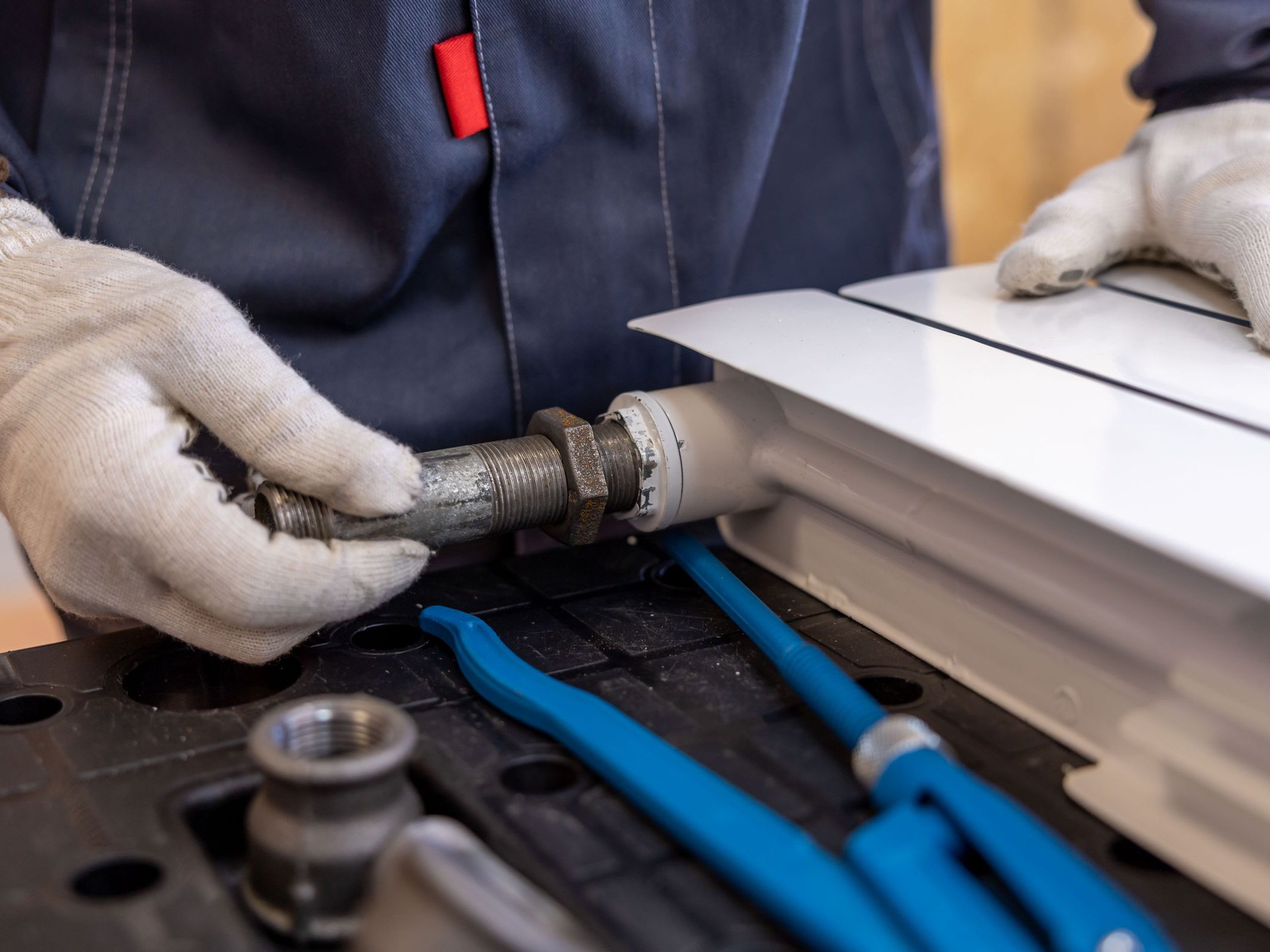 Heizungsmontage Monteur verschraubt eine Heizungsleitung mit Handschuhen – Heizungsmontage von SOS Gebäudetechnik